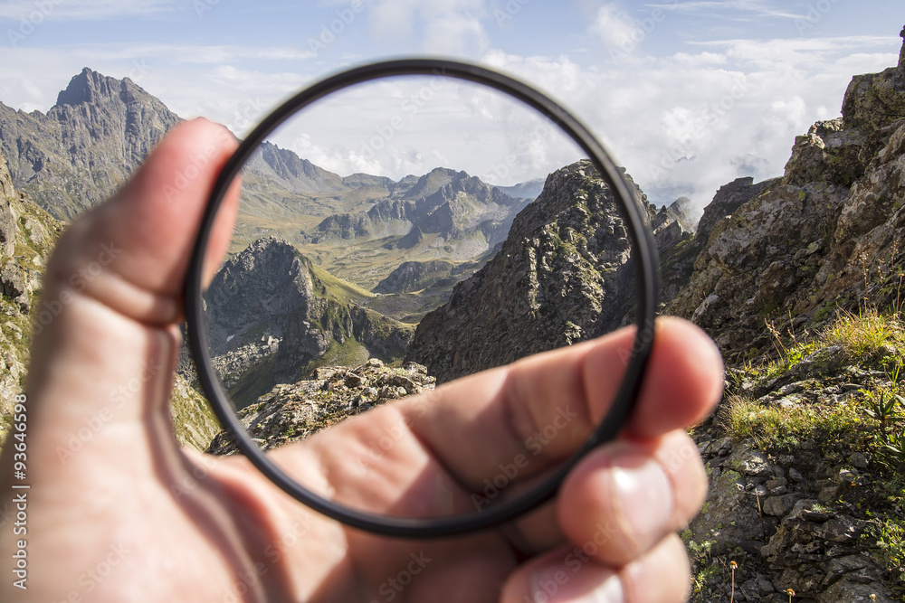 Hand puts a transparent clean protective UV filter to the camera, in the background a beautiful landscape and mountains